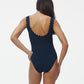 Model with long dark hair wears the Karla Colletto Ines Round Neck One Piece, featuring rick rack edging, shown from the back against a plain white background.