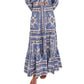A person in the Cara Cara Emilia Skirt—a blue and white placed print smocked maxi skirt—and matching top, barefoot in sandals, stands against a white background.