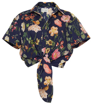 The Asbury Top by Cara Cara is a cropped, short-sleeve button-up shirt with a front tie bow, featuring a dark navy base with colorful floral and butterfly prints.