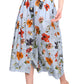 A person dons the Marge Skirt set from Cara Cara, featuring a blue floral print cotton poplin skirt with a matching waist-tied top and gold sandals, against a plain white backdrop.