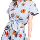 A person wearing the Asbury Top, a Cara Cara design, featuring a blue floral pattern with short sleeves and a front tie bow.