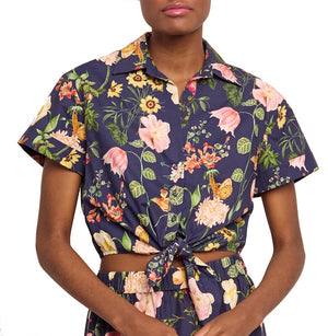 A person wears the Cara Cara Asbury Top—a colorful, floral short sleeve button-up tied in a bow at the waist—paired with matching high-waisted bottoms.
