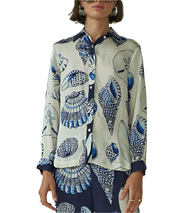 A woman wears the Carmen Shirt by Carolina K, featuring a blue and white seashell print—part of a striking collaboration with a South African artist.