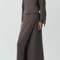 A person wears the Simkhai Natalia Sweater, a ribbed taupe collared top with Western-inspired detailing, styled with a matching fringed maxi skirt and pointed dark brown boots.