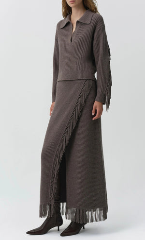 A person wears the Simkhai Natalia Sweater, a ribbed taupe collared top with Western-inspired detailing, styled with a matching fringed maxi skirt and pointed dark brown boots.