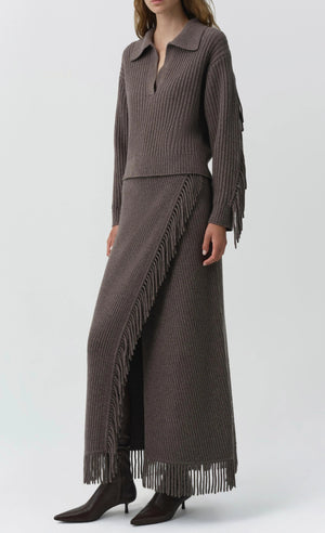 A person wearing a ribbed brown knit sweater and the Simkhai Casey Knit Skirt—a matching wool-cashmere blend fringed maxi skirt with a slit—paired with brown pointed boots.