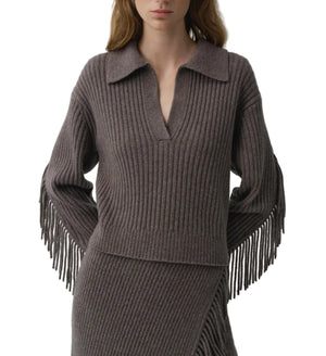 A woman wears the Natalia Sweater by Simkhai, a ribbed knit design with a collared V-neck and long fringe sleeves featuring Western-inspired detailing, paired with a matching ribbed skirt.