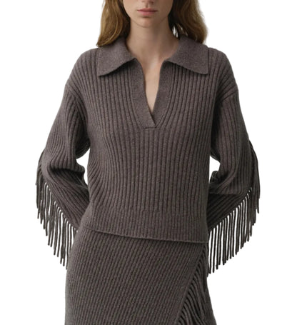A woman wears the Natalia Sweater by Simkhai, a ribbed knit design with a collared V-neck and long fringe sleeves featuring Western-inspired detailing, paired with a matching ribbed skirt.