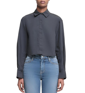 A person showcases the Simkhai Renata Cropped Shirt with blue jeans, standing against a plain white background.