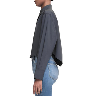 A person wearing the Simkhai Renata Cropped Shirt, which is a dark, long-sleeve button-down style, paired with light blue jeans featuring a tailored hemline, is viewed from the side against a plain white background.