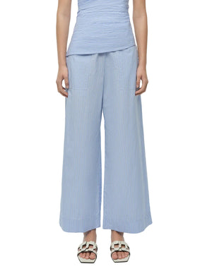 A person wearing Simkhai’s Arden Pull On Pant in light blue and white pinstripes, paired with a matching sleeveless top and white sandals, shown from shoulders to feet.