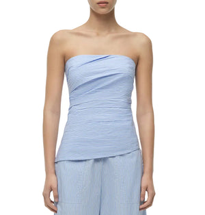 A woman wearing the Emerson Ruched Bustier Top by Simkhai in light blue cotton poplin with a subtle striped pattern, paired with matching wide-leg pants.