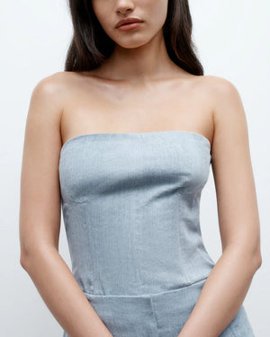 A woman stands against a plain white background with her arms relaxed in front of her, wearing the TWP Jillian Bustier, a strapless light blue dress.