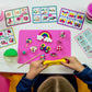 A child molds yellow playdough at a table with cards displaying clay models, finished figures, and containers of colored playdough from the Princess Clay & Play sculpting kit by Floss and Rock.