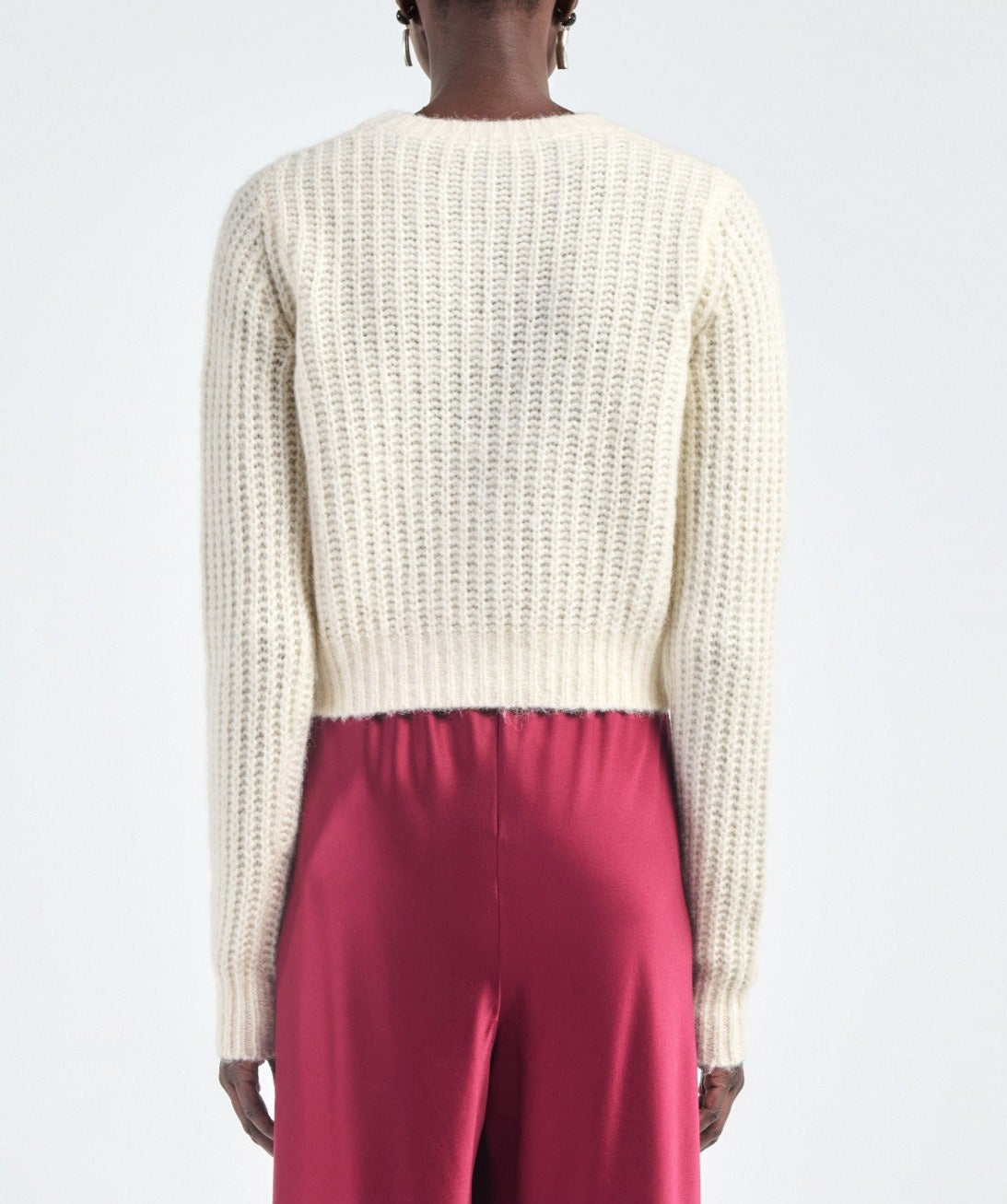 A person is shown from the back wearing the Maria McManus Shrunken V Cardigan in a cream wool-cashmere blend and high-waisted pink pants against a plain background.