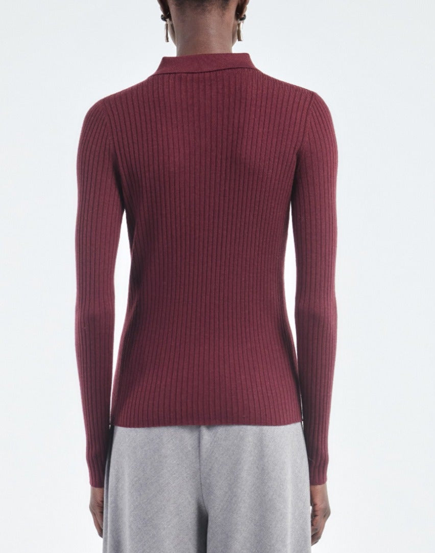 A person is shown from the back against a plain white background, wearing the Maria McManus Single Button Polo, a slim-fitting, long-sleeve ribbed burgundy sweater, paired with light gray pants.