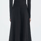 A person faces away, wearing the Maria McManus Button Front Dress—an ankle-length, long-sleeved black dress made from FSC-certified viscose—with white heeled shoes against a plain light backdrop.