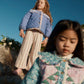 Two young girls stand outdoors on a rocky slope, both wearing patterned jackets and the Louise Misha Girls’ Ysalia Sweatpant with an elasticated waist, under a clear blue sky.