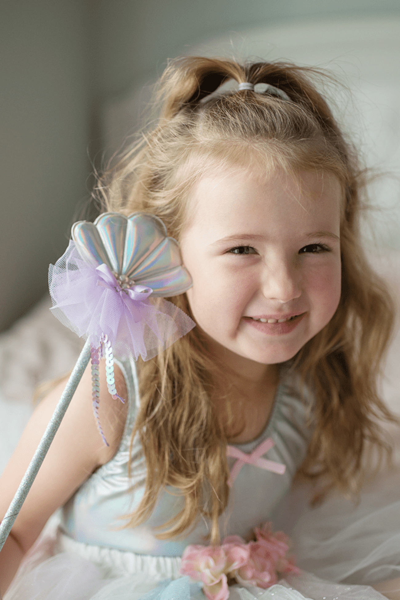 A girl smiling with a Great Pretenders Mermaid Wand in an under-the-sea setting.