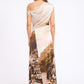 A woman stands facing away, wearing the Staud Phare Silk Maxi Dress featuring a one-shoulder neckline and a scenic city and coastline print on the skirt.