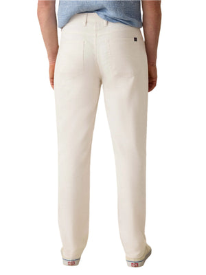 A person stands facing away, showing only their lower back and legs in Faherty's Movement™ Linen 5-Pocket Pant in off-white, paired with a light blue shirt and white slip-on shoes.