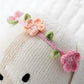 A close-up of Cuddle + Kind’s Charlotte the Dog - Regular 20" wearing a pink and peach wildflowers headband with green leaves, set against a white textured background.