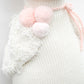 A close-up of Cuddle + Kind’s Harlow the Swan - Little 13": a white knitted sweater with a textured patch and three pink pom-poms tied at the back, capturing a sense of lightness and brave wings.