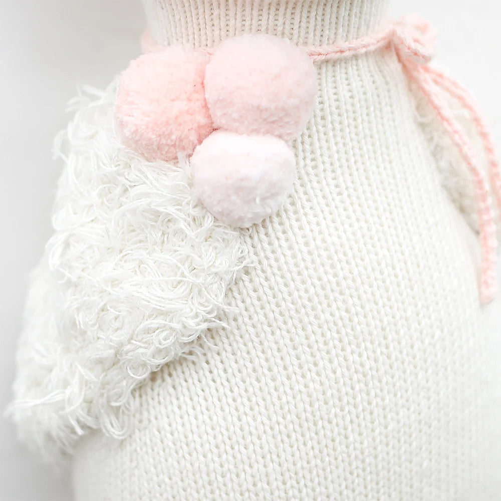 Close-up of Harlow the Swan - Regular 20" by Cuddle + Kind, a knitted white plush with textured fluffy detail and three pastel pink pom-poms tied at the neck, evoking a dreamy, whimsical feel.