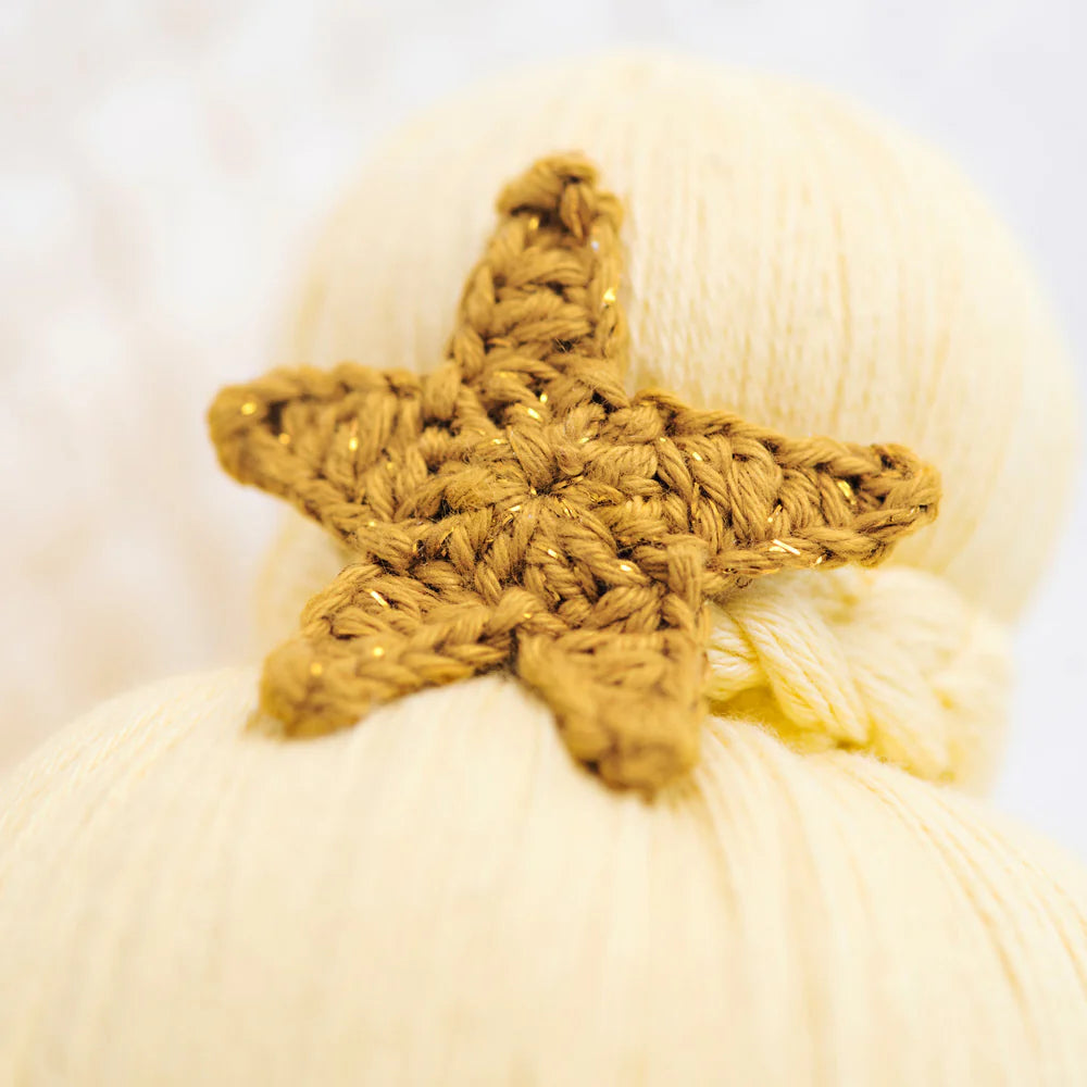 Skye the Mermaid - Regular 20" by Cuddle + Kind, featuring a yellow crocheted star, is displayed on a bundle of pale yellow yarn—perfect for an ocean toy set.