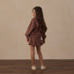 A young girl wearing the Rylee & Cru Girls’ Half Zip Sweatshirt stands on a wooden floor, facing away but looking back over her shoulder toward the camera.