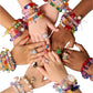 Several hands of different skin tones are grouped together, each adorned with vibrant beaded creations and sparkling rings, showcasing the creativity inspired by the Super Smalls Make It Super DIY Bead Kit from Super Smalls.