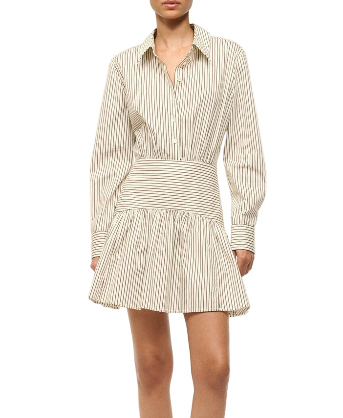 A woman wears the Staud Rocco Mini Dress, featuring beige and white vertical stripes, a collared neckline, and a flared A-line mini skirt.