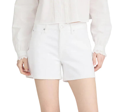 A person wears Frame’s The Long Hang Short, a relaxed-fit white high-waisted short with a 4½” inseam, styled with a white long-sleeve blouse and standing with hands by their sides.