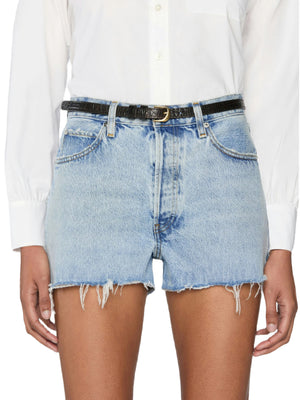 A person wears The Dare Short by Frame—mid-rise, light blue distressed denim shorts with frayed hems—a white button-up shirt, and a black belt.