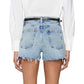 Model wears The Dare Short by Frame—light blue, mid-rise denim cut-offs—paired with a white long-sleeve shirt, seen from the back for a subtle vintage vibe.