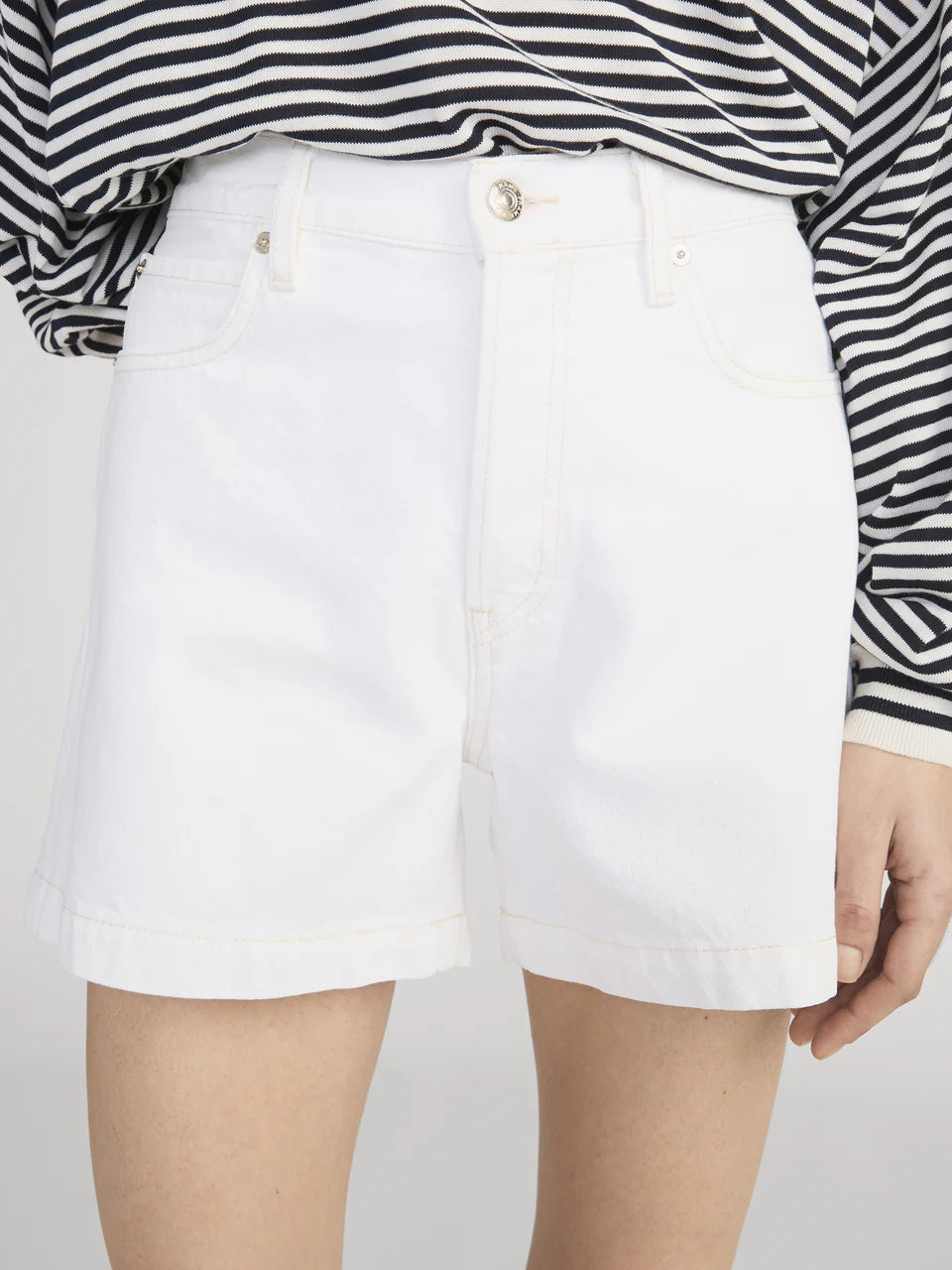 A person wears a black and white striped long-sleeve shirt tucked into Frame’s The Everyday Short—pure cotton, high-rise tailored shorts with a 4" inseam.