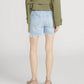 Person wearing a green jacket and Frame’s The Everyday Short—pure cotton, high-rise, 4" inseam with frayed hems—paired with beige low-heeled shoes, standing against a plain background, viewed from behind.