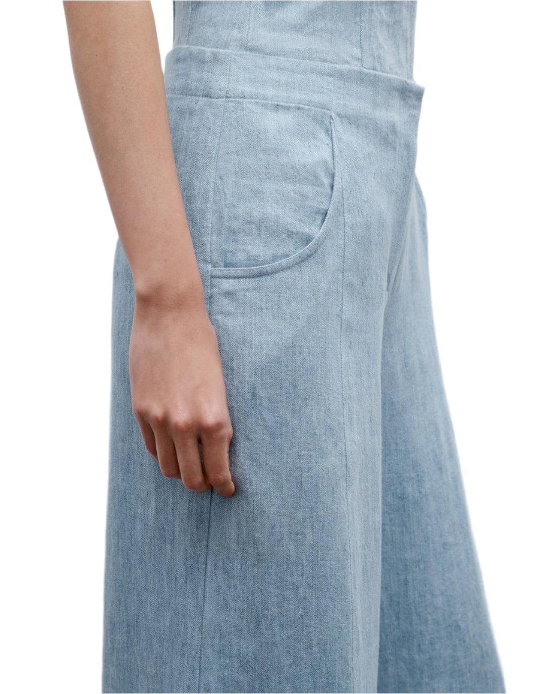 A person wearing the TWP Demi Hemp Denim Pant in light blue, a high-rise, wide-leg style, stands with their left arm relaxed by their side, shown from waist to mid-thigh.