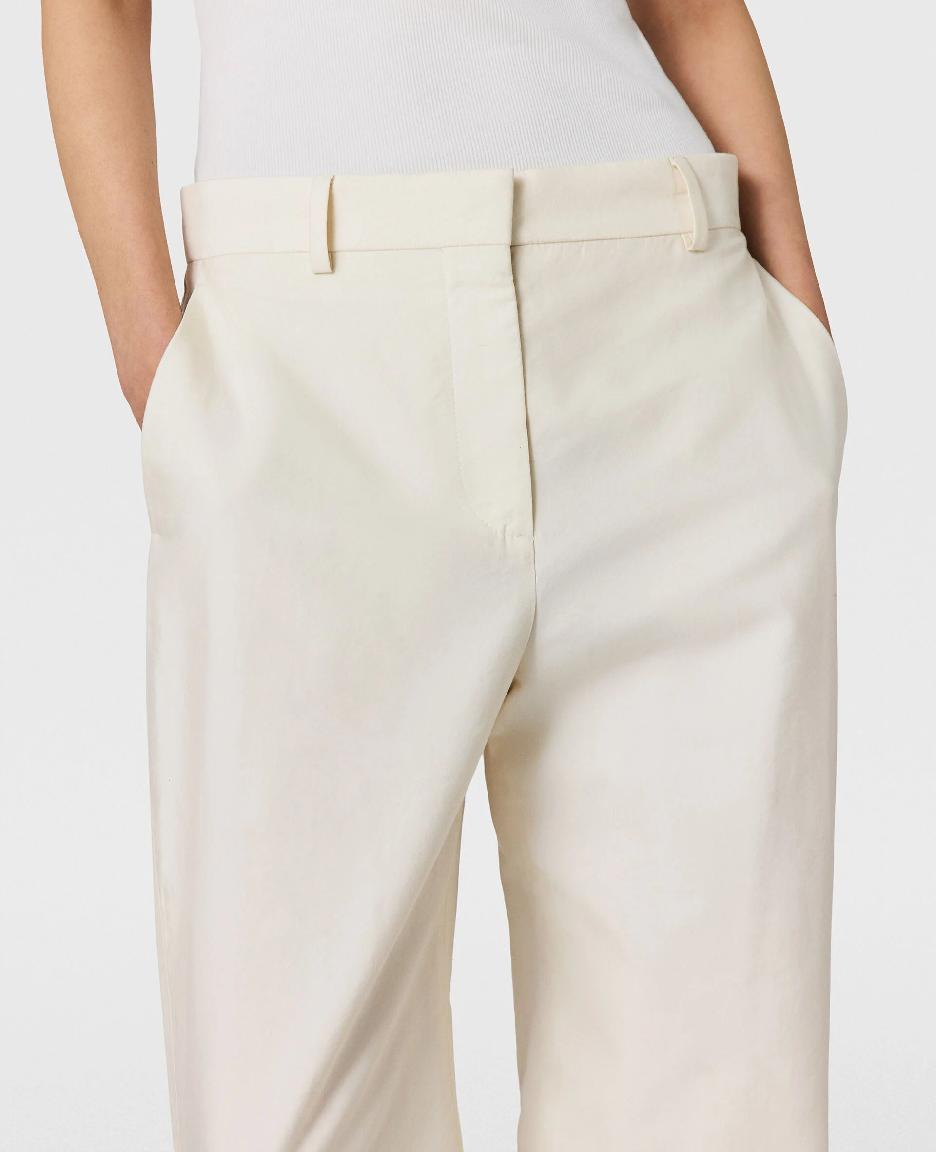 Model wears Stella McCartney Washed Cotton Straight Trousers in cream, styled with a white sleeveless top, hands in pockets, shown from waist to upper thighs.