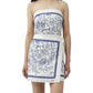 A woman wears the Simkhai Darbie Linen Mini Dress, a white wrap mini dress with blue seashell prints and a matching waist belt.