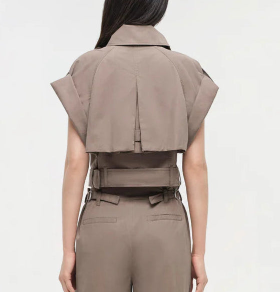 A woman is seen from the back wearing the Simkhai Axel Top, a taupe, short-sleeve cropped jacket with a utilitarian notch collar and vented back detail, paired with matching high-waisted pants.