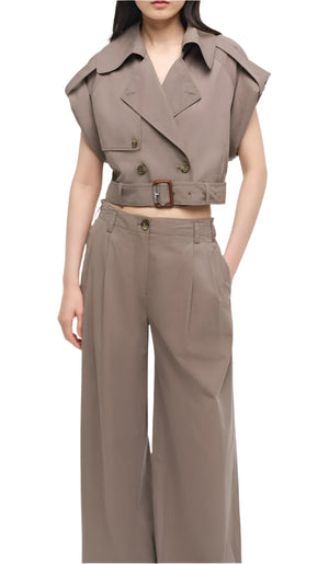 A woman wearing Simkhai's Haydin Wide Leg Pant with side pockets, paired with a taupe belted cropped trench vest, stands with one hand in her pocket.