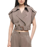 A woman wears the Axel Top by Simkhai—a taupe, short-sleeved, cropped trench with utilitarian notch collar, button details, and belt—paired with matching high-waisted pants.