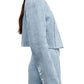 A woman wears TWP’s “Drink At Costes,” a light blue long-sleeved cropped blazer with shoulder pads, four white cuff buttons, and a matching high-waisted skirt.