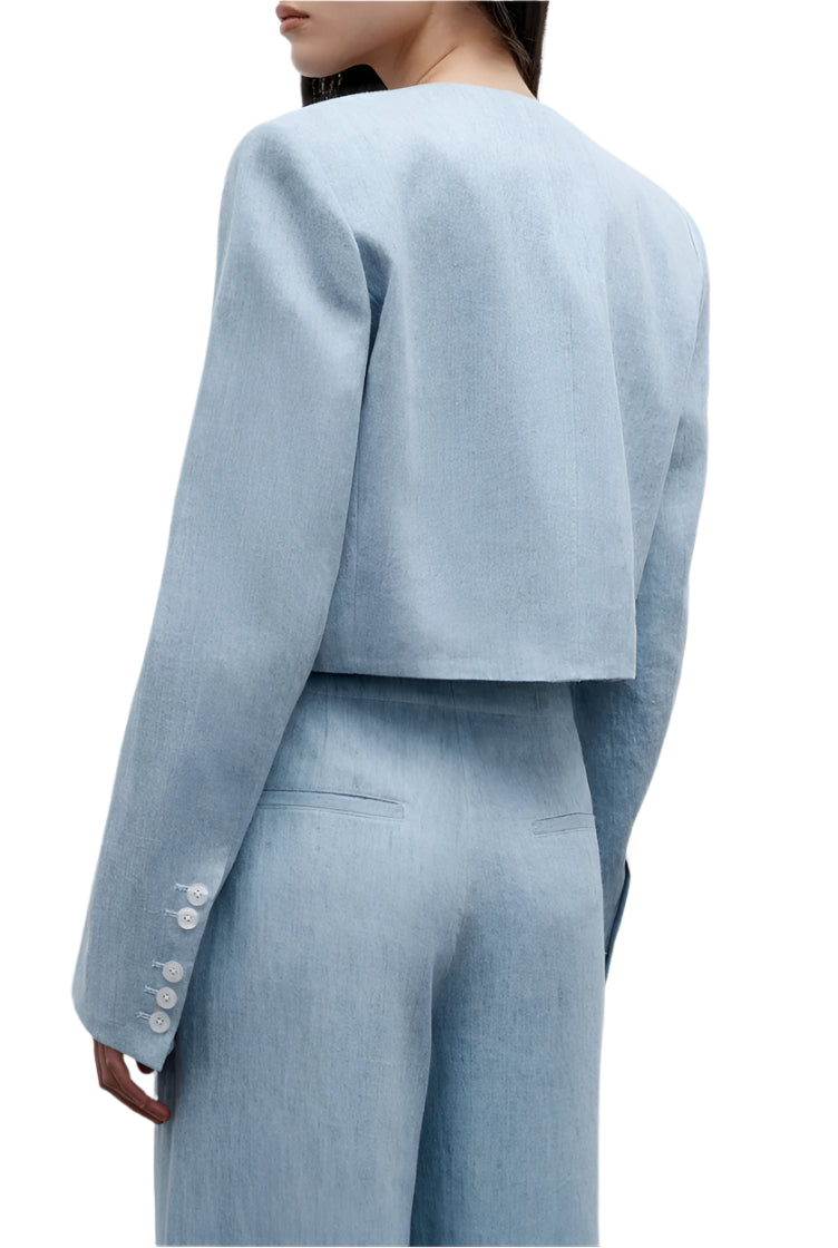 A person is seen from the back wearing TWP's "Drink At Costes" light blue washed hemp denim suit, featuring a cropped blazer with shoulder pads and high-waisted pants.