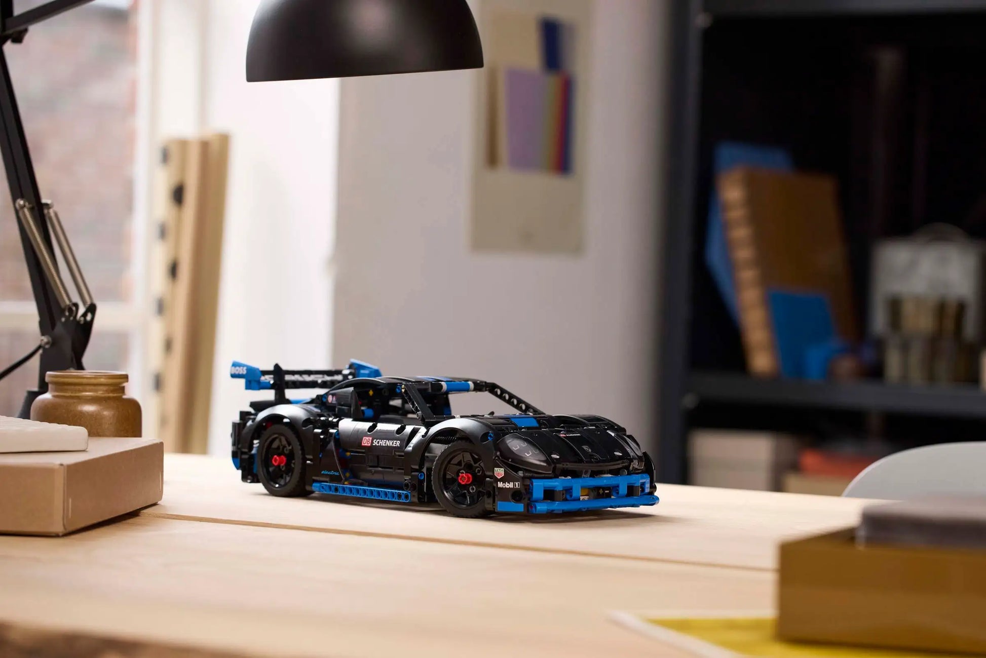A LEGO® Technic™ Porsche GT4 e-Performance Race Car by Legos - Toyhouse sits on a wooden desk in a modern, well-lit room with books and folders in the background.