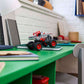The LEGO® Technic™ Monster Jam™ ThunderROARus™ Pull-Back toy by Legos - Toyhouse is placed atop a stack of notebooks on a green desk in a study area filled with books, a lamp, and stationery items.
