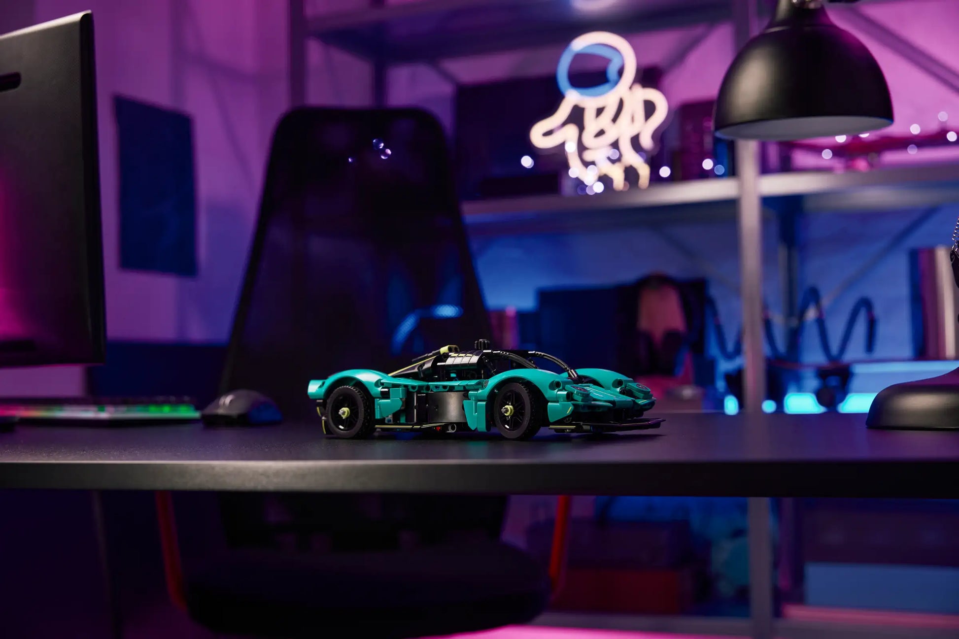 A LEGO® Technic™ Aston Martin Valkyrie by Legos - Toyhouse sits on a desk in a modern workspace with neon lighting and shelves in the background.