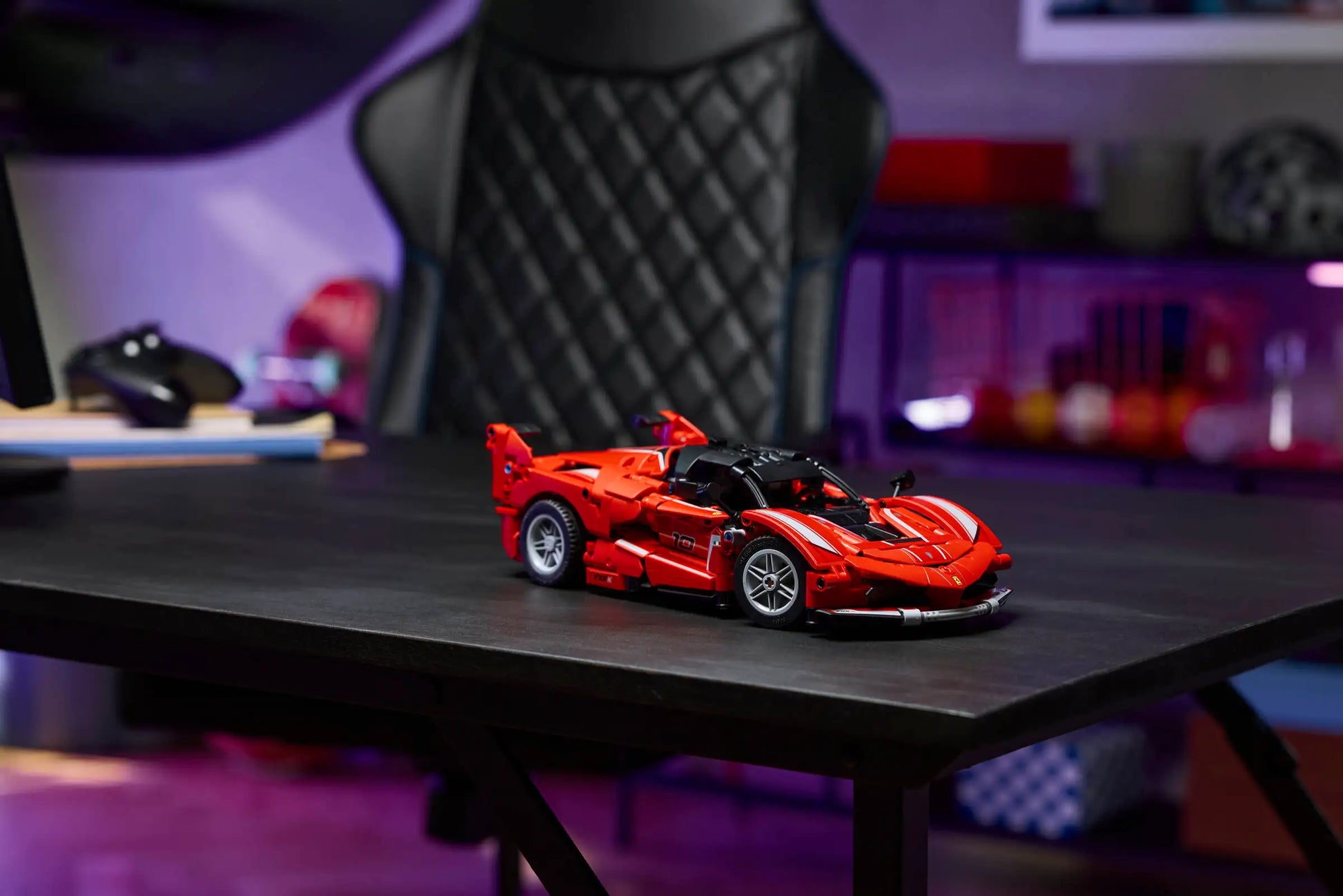 A LEGO® Technic™ Ferrari FXX K model by Legos - Toyhouse sits on a black desk in a modern room, with a black office chair and shelves in the background.