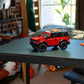 A LEGO® Technic™ Ford Bronco® SUV by Legos - Toyhouse is displayed on a dark green table in a room filled with shelves, sports equipment, and natural light.